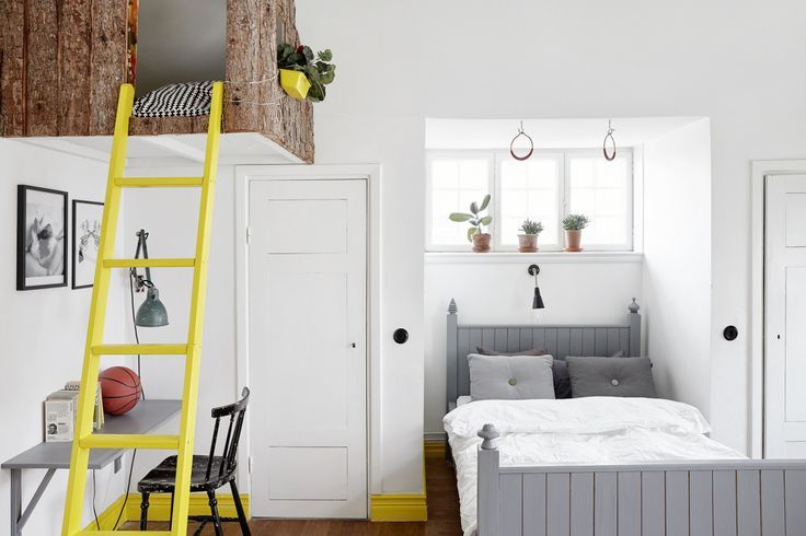 Stock image of a bedroom with a gray bed and yellow ladder going up to a raised loft area. 