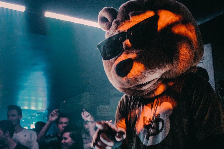 A DJ wearing a bear costume playing to a crowd inside a club.