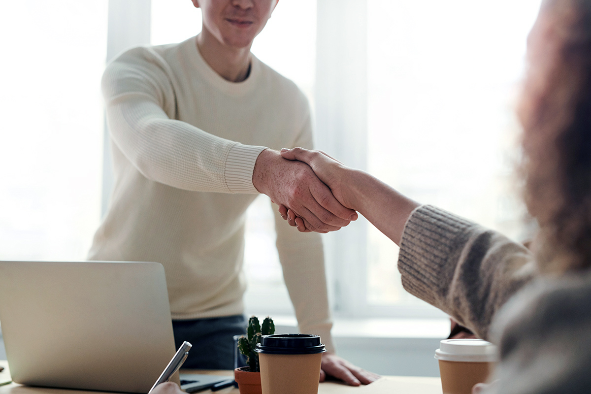 Two people shaking hands at a negotiation table