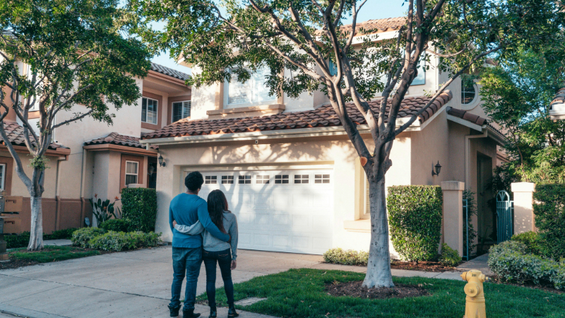 A couple standing in front of a house on a sunny day.