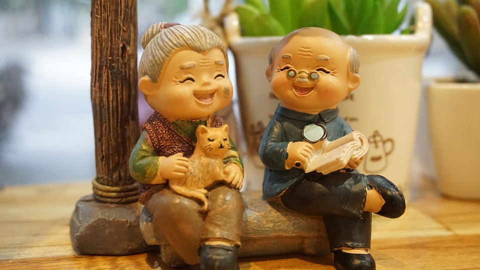 a figurine of an senior asian man and woman sitting laughing with a cat and book, happy in retirement from investing in Cash Offer Canada