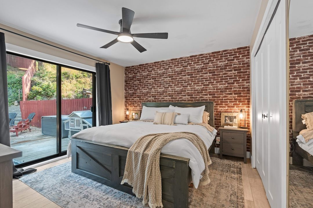 Main-floor primary bedroom with brick feature wall and deck access at 3925 Highland Park Crescent