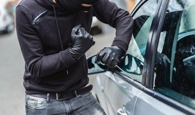 Person in a black jacket and black leather gloves breaking into a car.